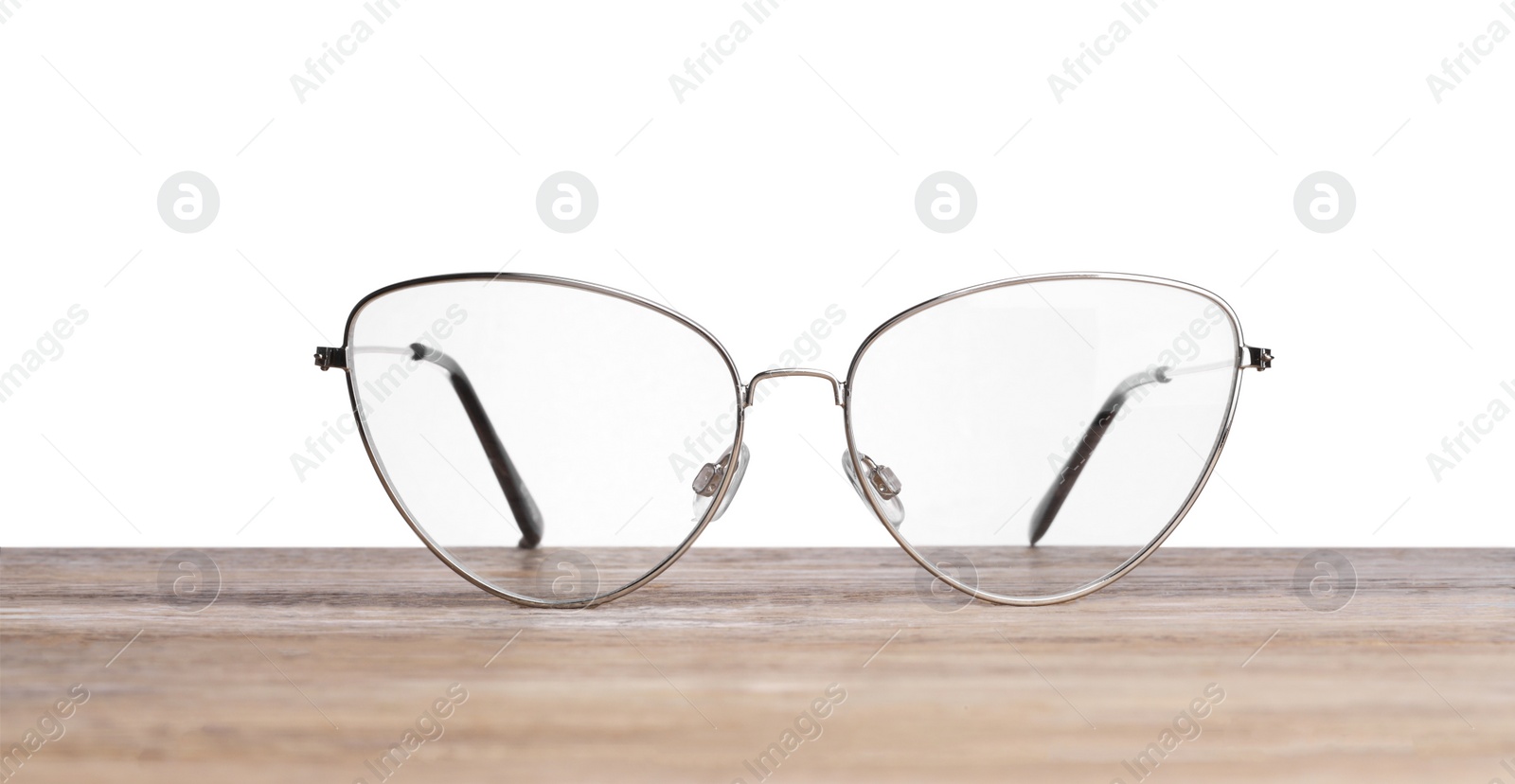 Photo of Stylish glasses with metal frame on wooden table against white background