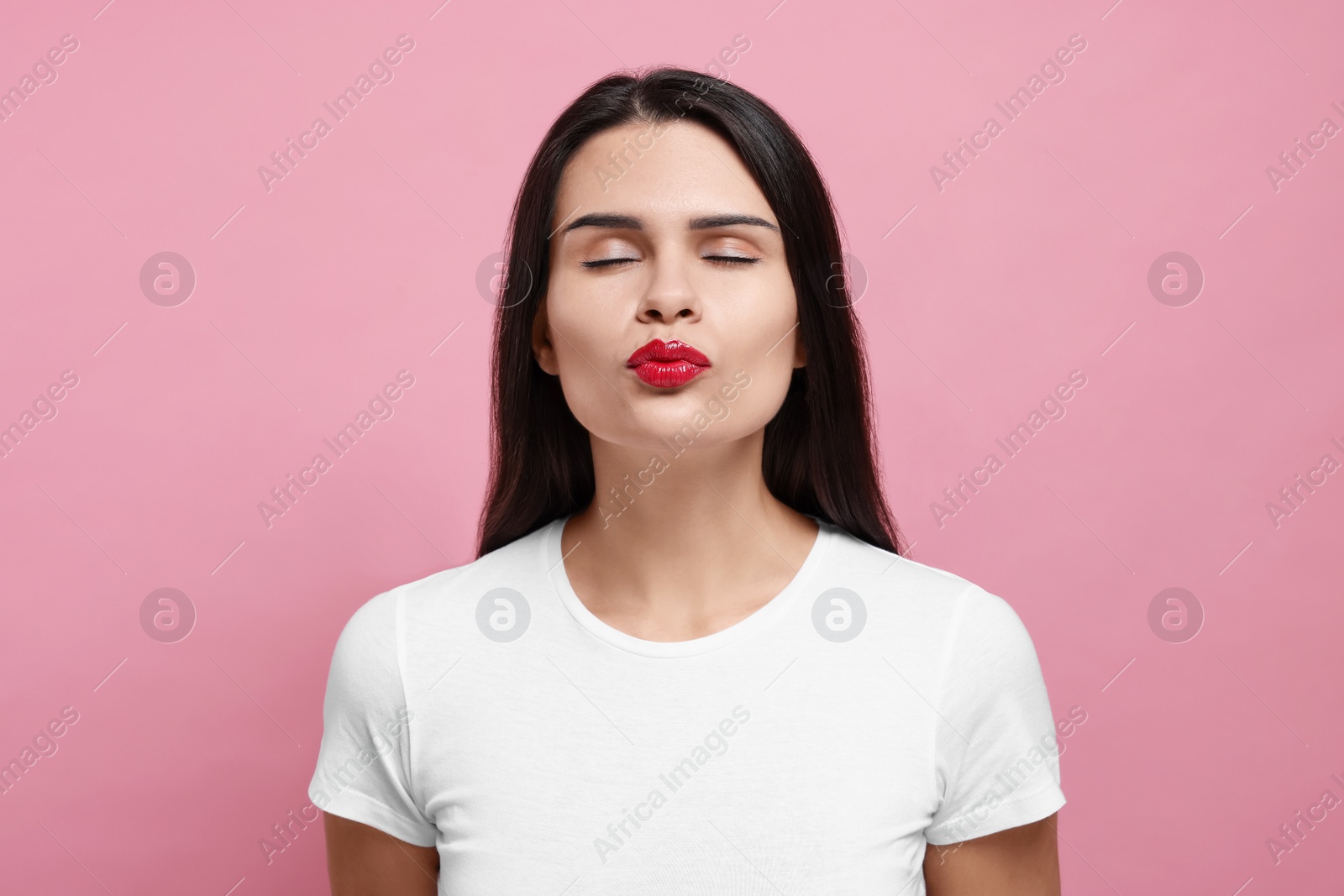 Photo of Beautiful young woman giving kiss on pink background