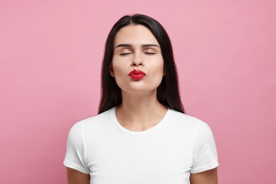 Photo of Beautiful young woman giving kiss on pink background