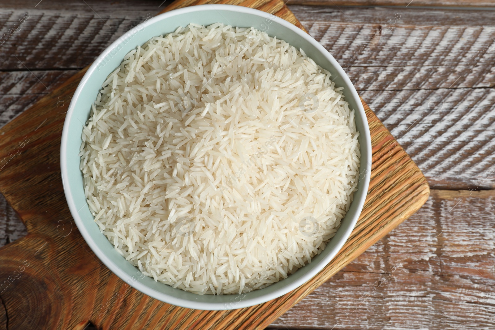 Photo of Raw basmati rice in bowl on wooden table, top view