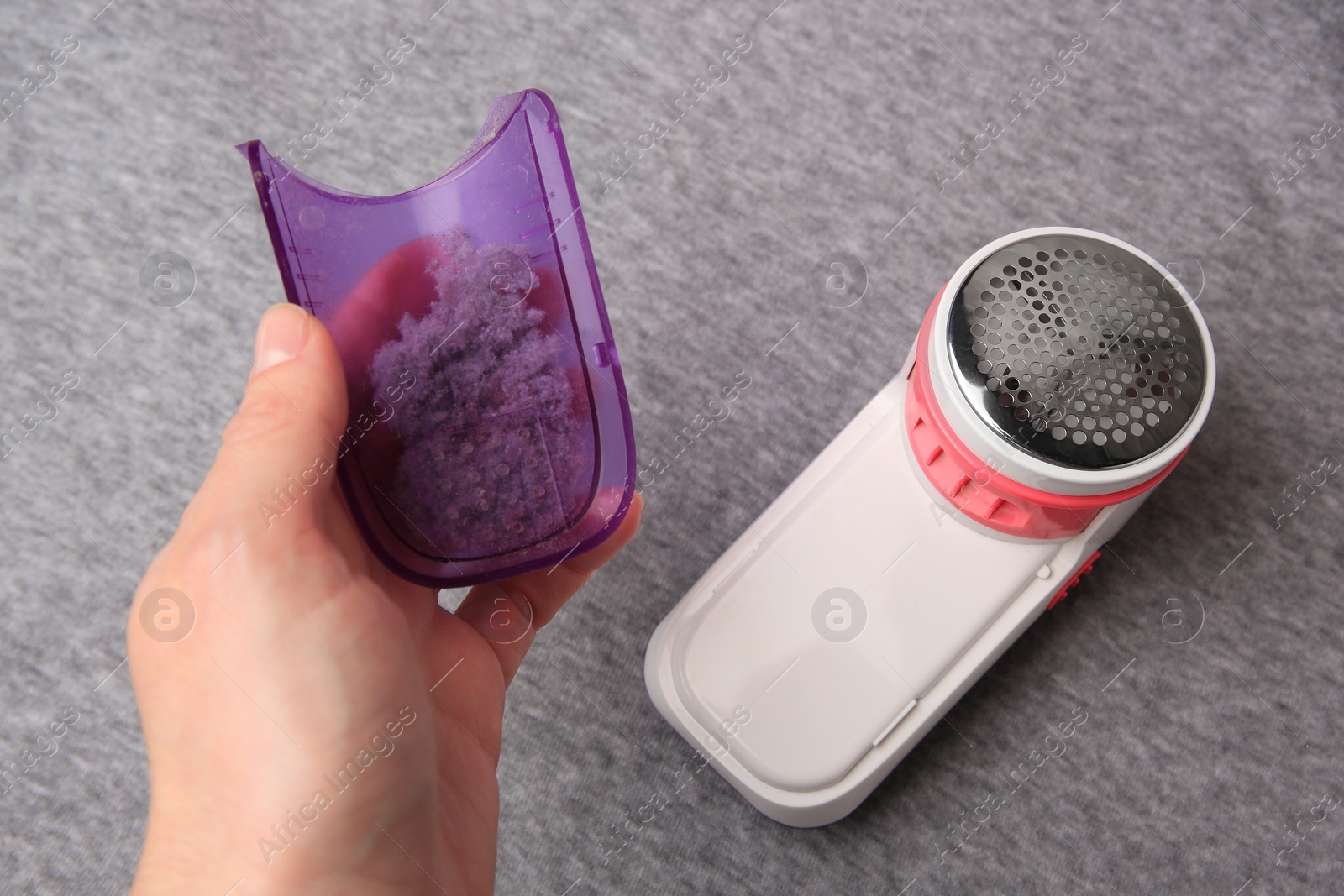 Photo of Woman holding fluff collector with lint of fabric shaver near light grey cloth, closeup