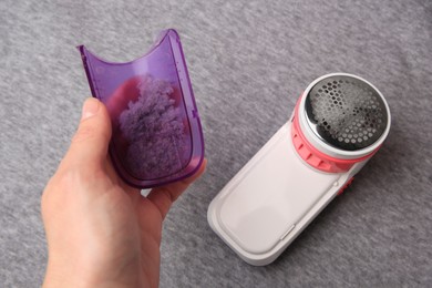 Photo of Woman holding fluff collector with lint of fabric shaver near light grey cloth, closeup