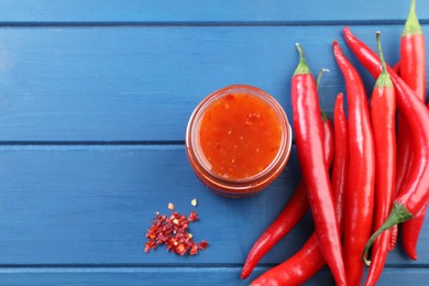 Photo of Spicy chili sauce in jar and peppers on blue wooden table, flat lay. Space for text