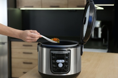 Young woman preparing food with modern multi cooker in kitchen