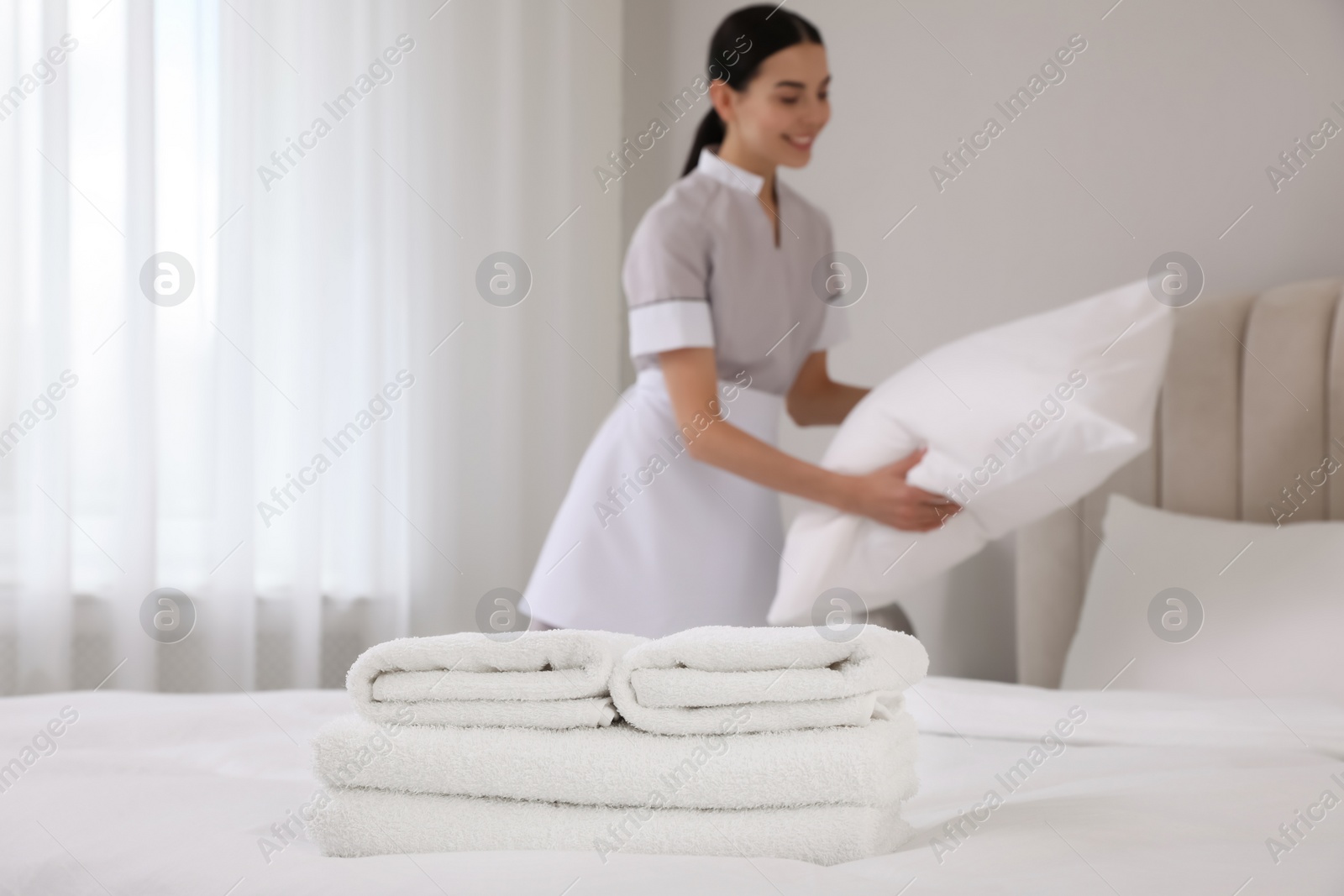 Photo of Chambermaid making bed in hotel room, focus on fresh towels. Space for text