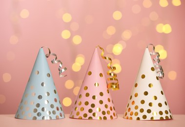 Photo of Beautiful party hats with streamers on pink table against blurred festive lights