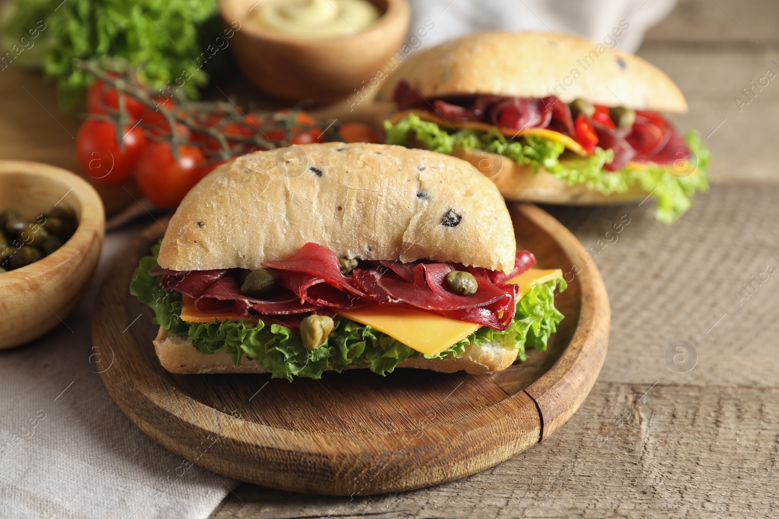 Photo of Delicious sandwiches with bresaola, cheese and lettuce served on wooden table, closeup
