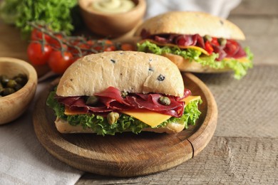 Photo of Delicious sandwiches with bresaola, cheese and lettuce served on wooden table, closeup