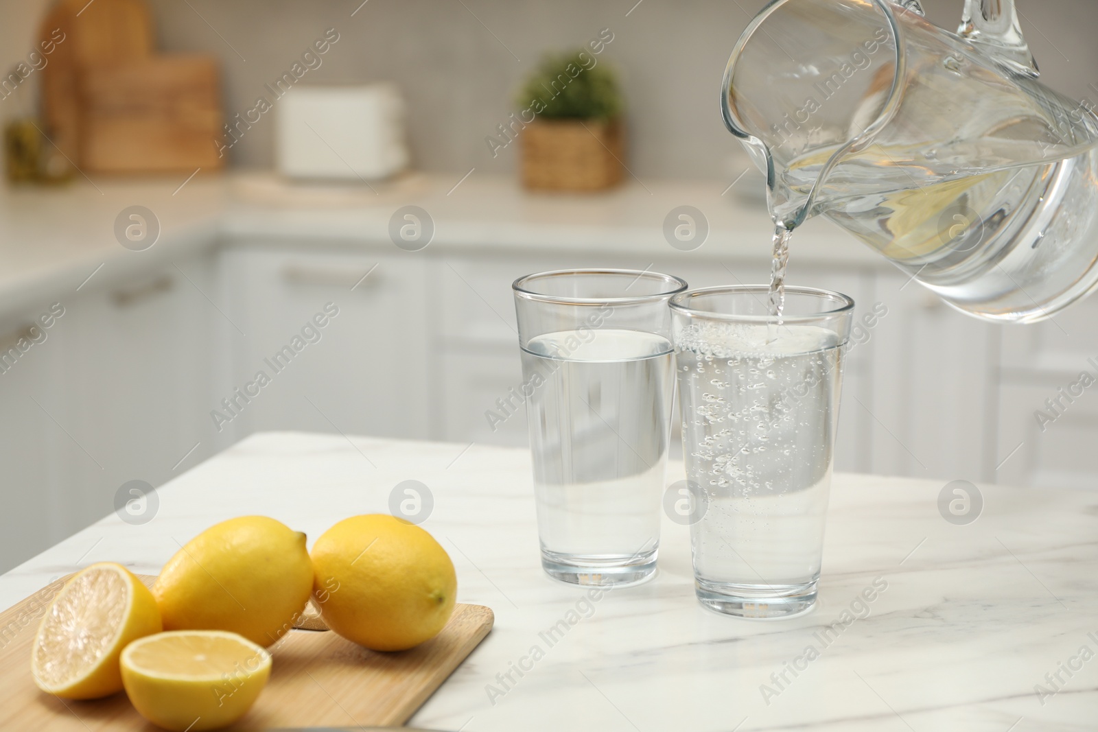 Photo of Pouring water from jug into glass on white table in kitchen, closeup