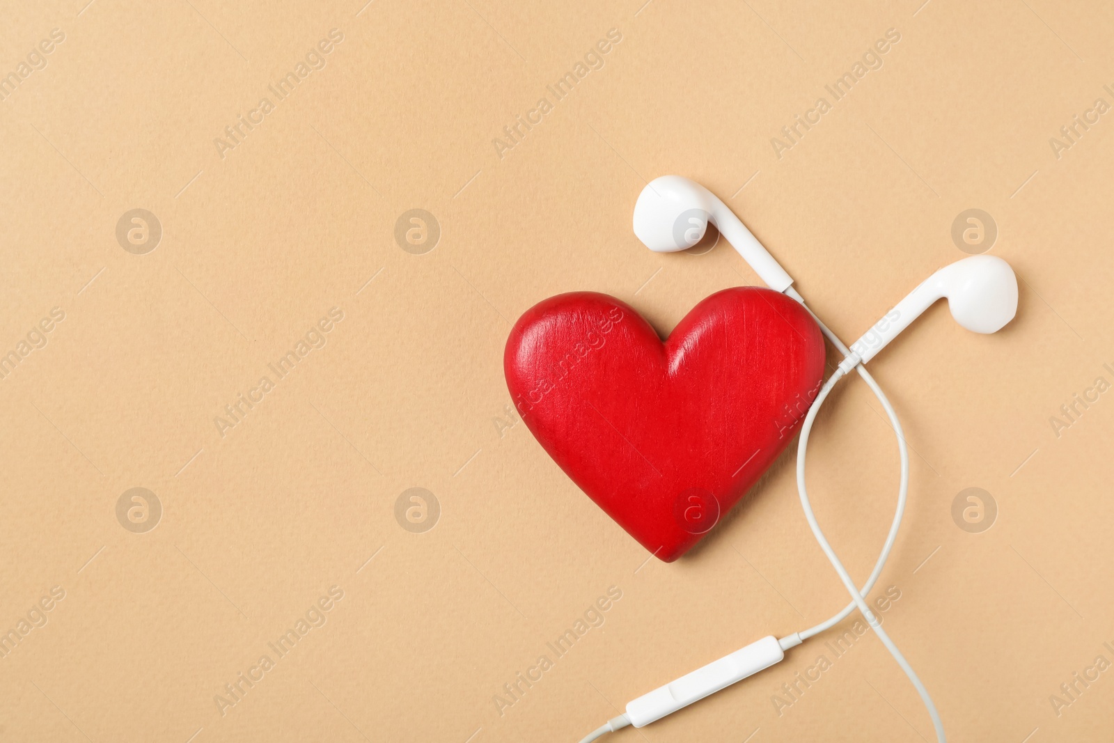 Photo of Modern earphones and red heart on beige background, flat lay with space for text. Listening love music songs