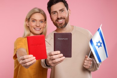 Immigration. Happy couple with passports and flag of Israel on pink background, selective focus