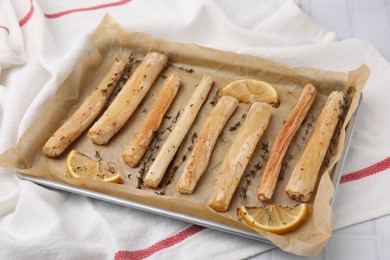 Photo of Baking tray with cooked salsify roots, lemon and thyme on table