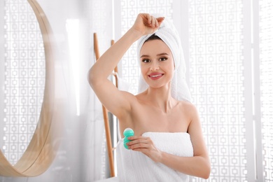 Photo of Beautiful young woman applying deodorant after shower in bathroom