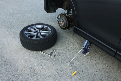 Car lifted by scissor jack and new wheel on asphalt outdoors. Tire puncture