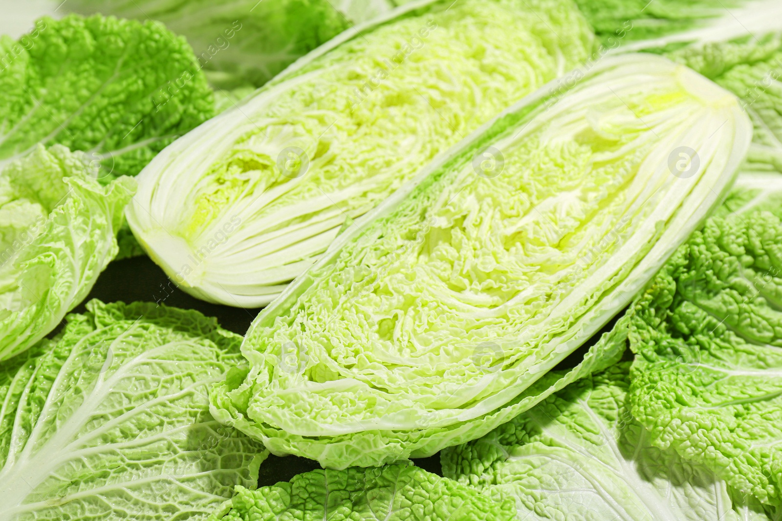 Photo of Halves of fresh Chinese cabbage and green leaves on table, closeup