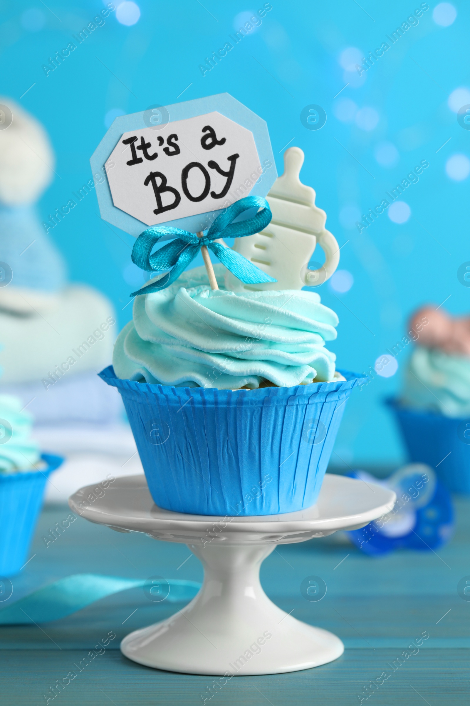Photo of Beautifully decorated baby shower cupcake for boy with cream and topper on light blue wooden table