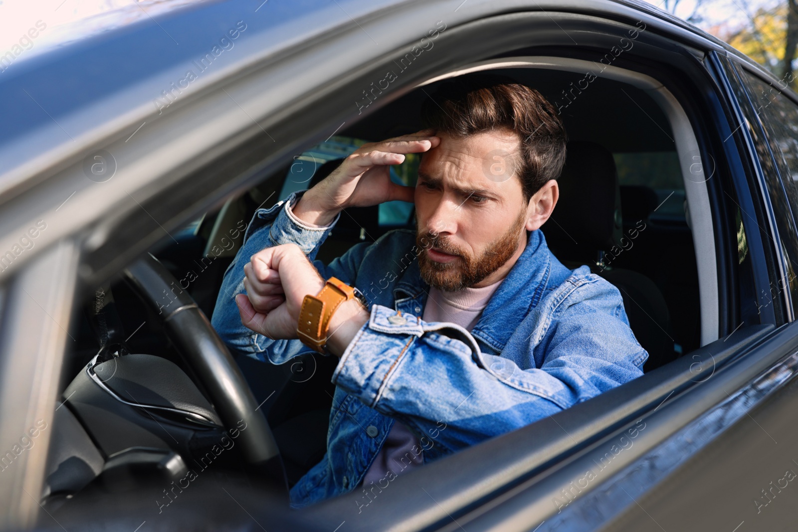 Photo of Emotional man checking time on watch in car. Being late concept