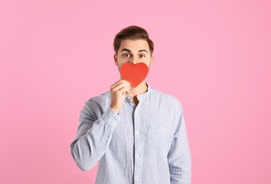 Portrait of young man with paper heart on color background