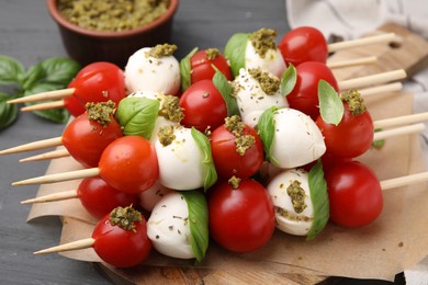 Photo of Caprese skewers with tomatoes, mozzarella balls, basil and pesto sauce on grey table, closeup