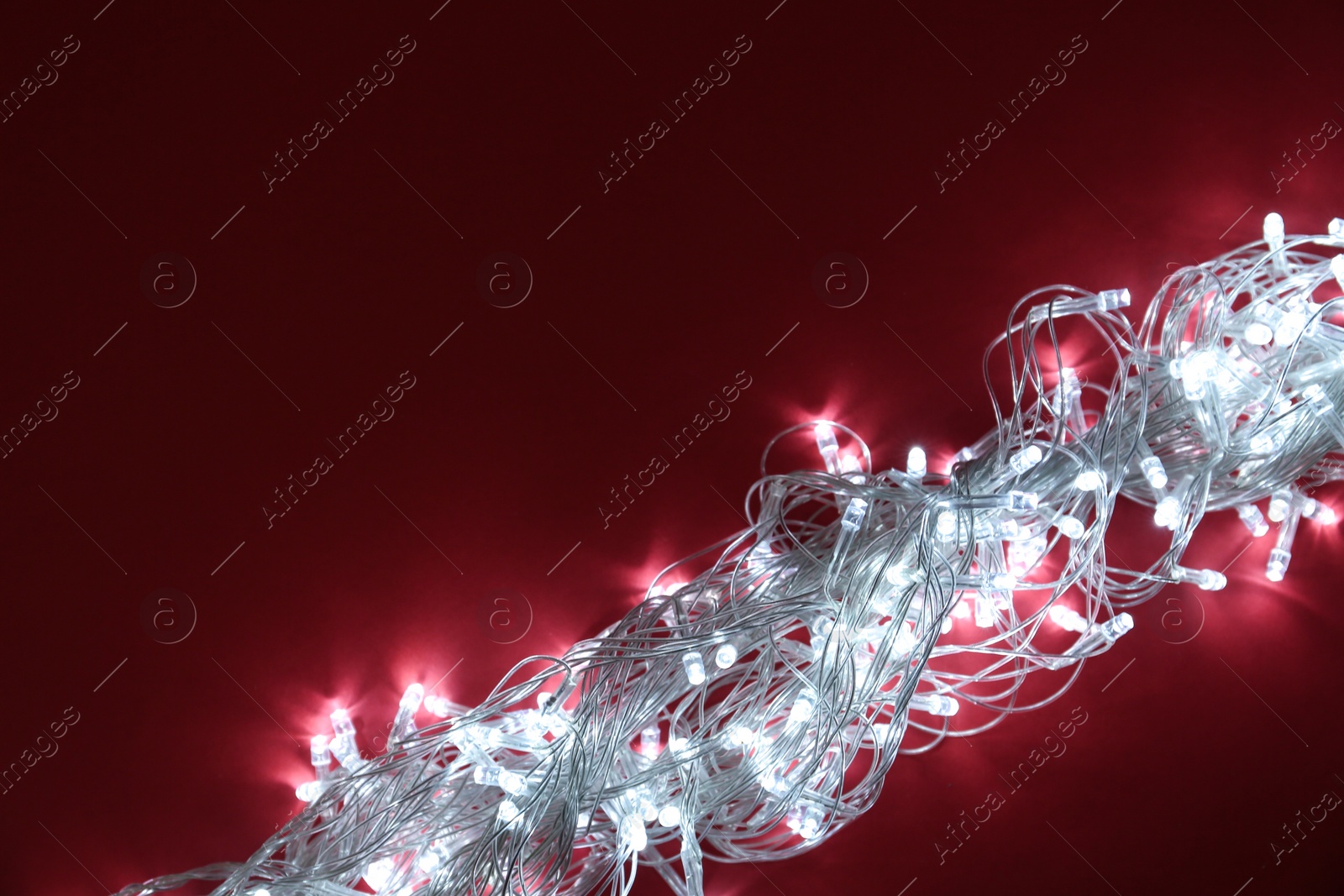 Photo of Glowing Christmas lights on burgundy background, top view. Space for text