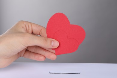 Woman putting red hearts into slot of donation box against grey background, closeup