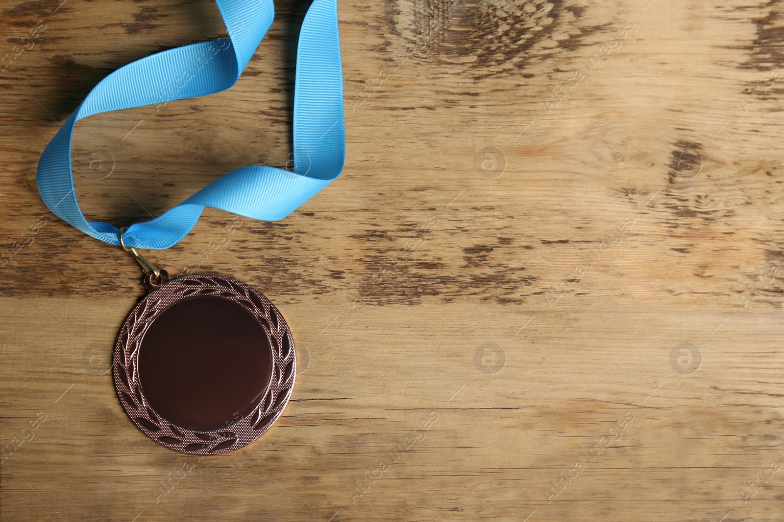 Photo of Bronze medal with light blue ribbon on wooden background, flat lay. Space for design
