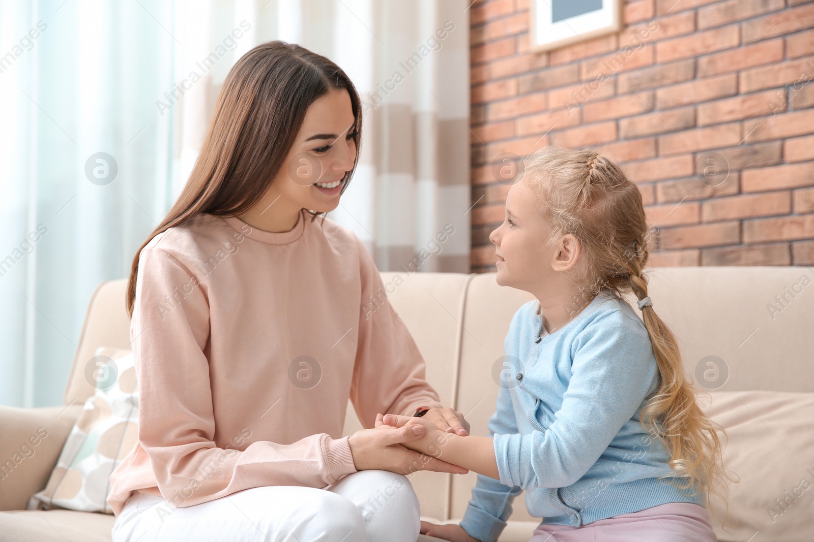 Photo of Young woman checking little girl's pulse with fingers at home