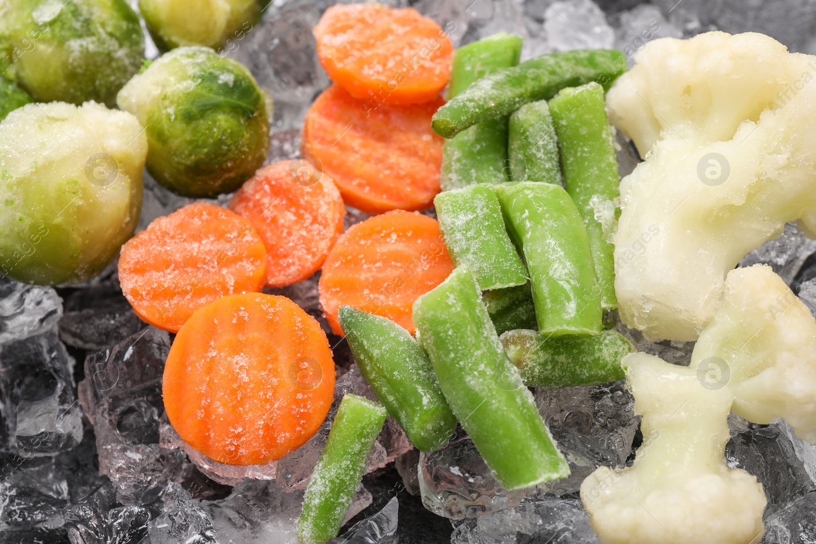 Photo of Different frozen vegetables and ice on black table, closeup