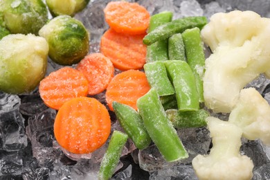 Different frozen vegetables and ice on black table, closeup