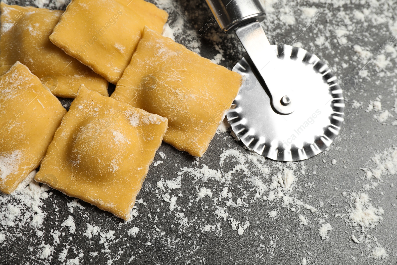 Photo of Ravioli and cutter on grey table, above view. Italian pasta