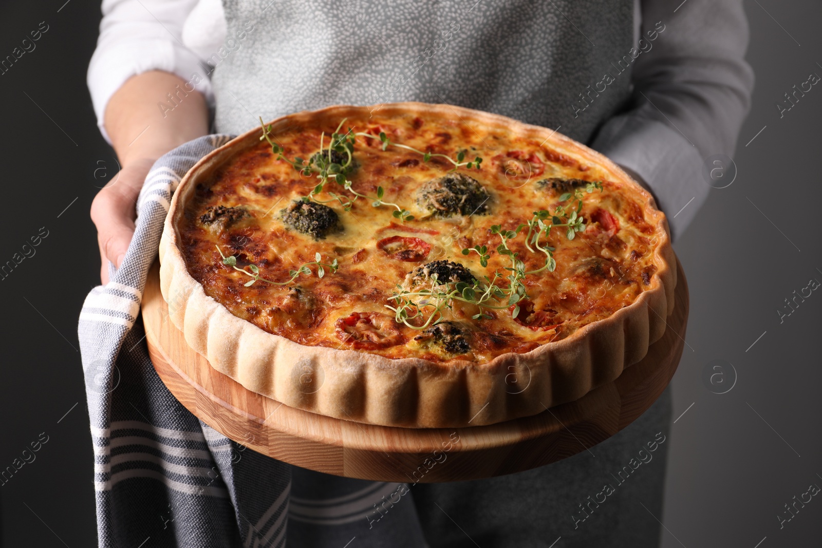 Photo of Woman holding delicious homemade vegetable quiche on light gray background, closeup