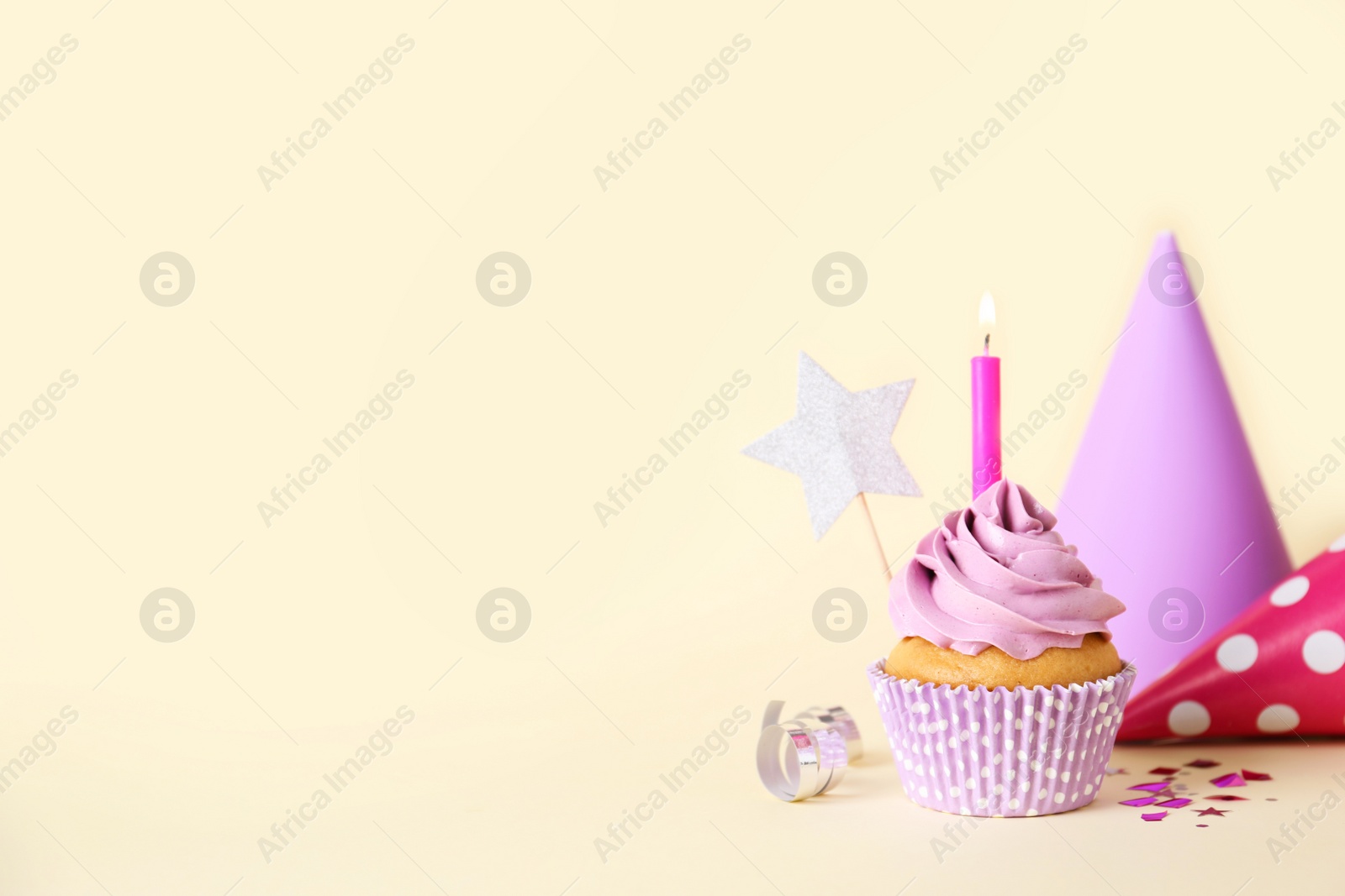 Photo of Delicious birthday cupcake with burning candle and party decor on beige background, space for text