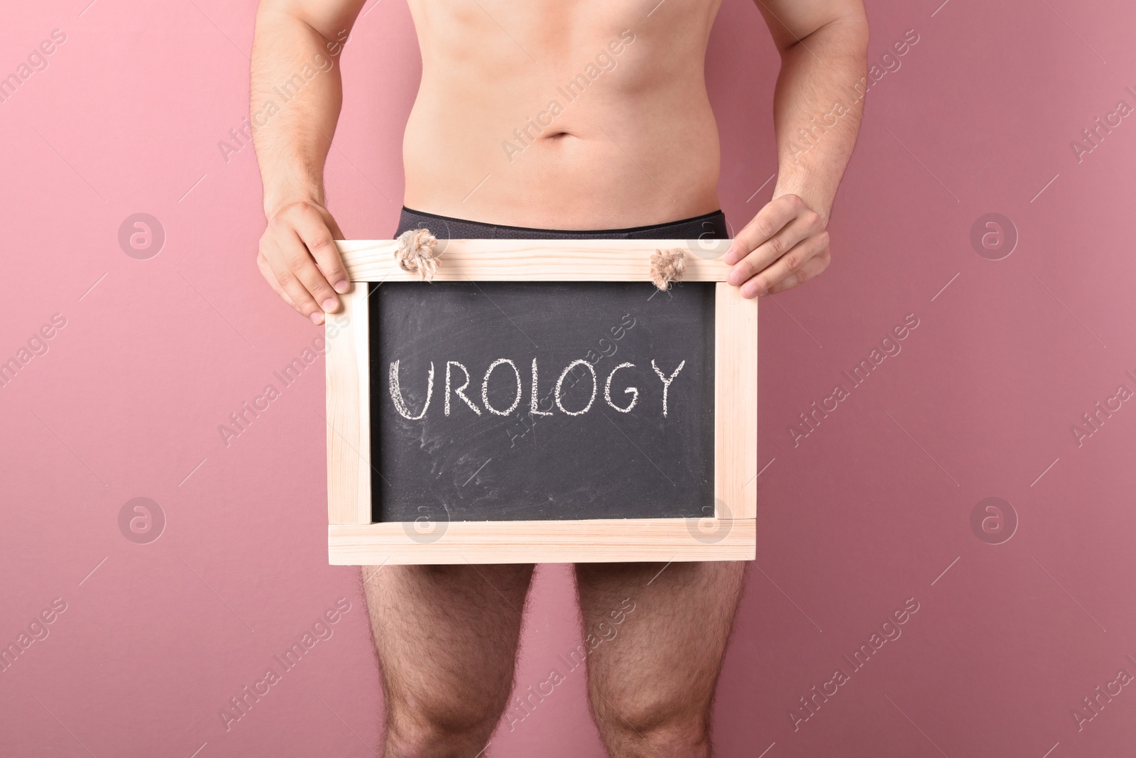 Photo of Young man holding chalkboard with word UROLOGY on color background