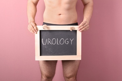 Photo of Young man holding chalkboard with word UROLOGY on color background