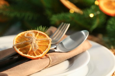 Photo of Festive place setting with beautiful dishware, fabric napkin and dried orange slice for Christmas dinner on table, closeup