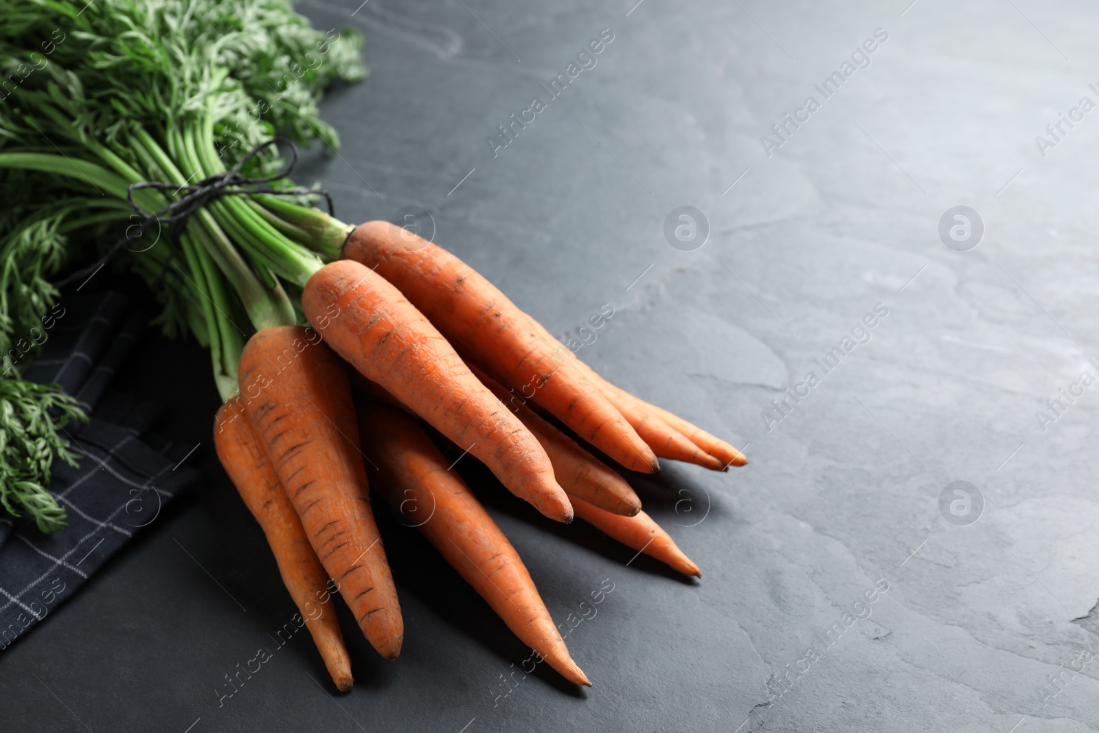 Photo of Bunch of tasty raw carrots on black slate table, closeup. Space for text