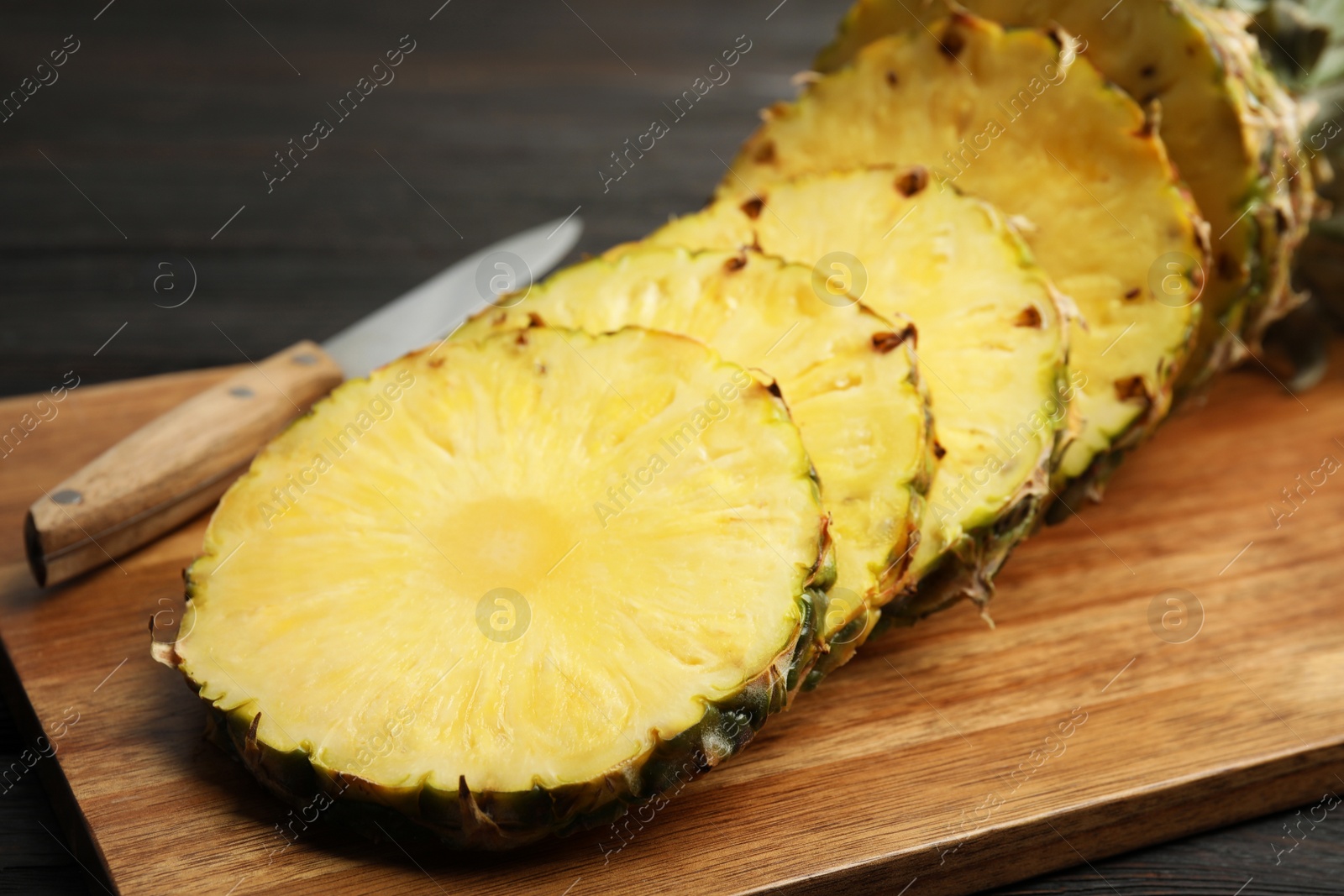 Photo of Tasty cut pineapple and knife on wooden board, closeup