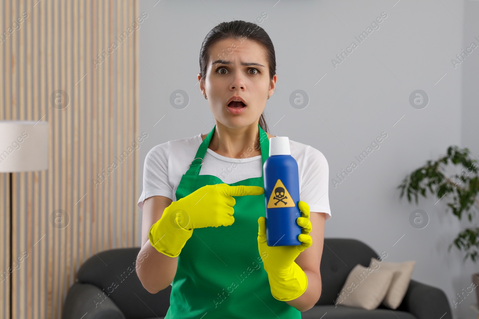 Photo of Woman showing bottle of toxic household chemical with warning sign indoors