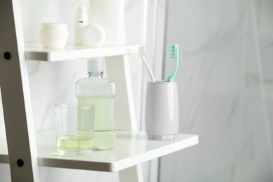 Photo of Bottle and glass with mouthwash on white shelf indoors, space for text