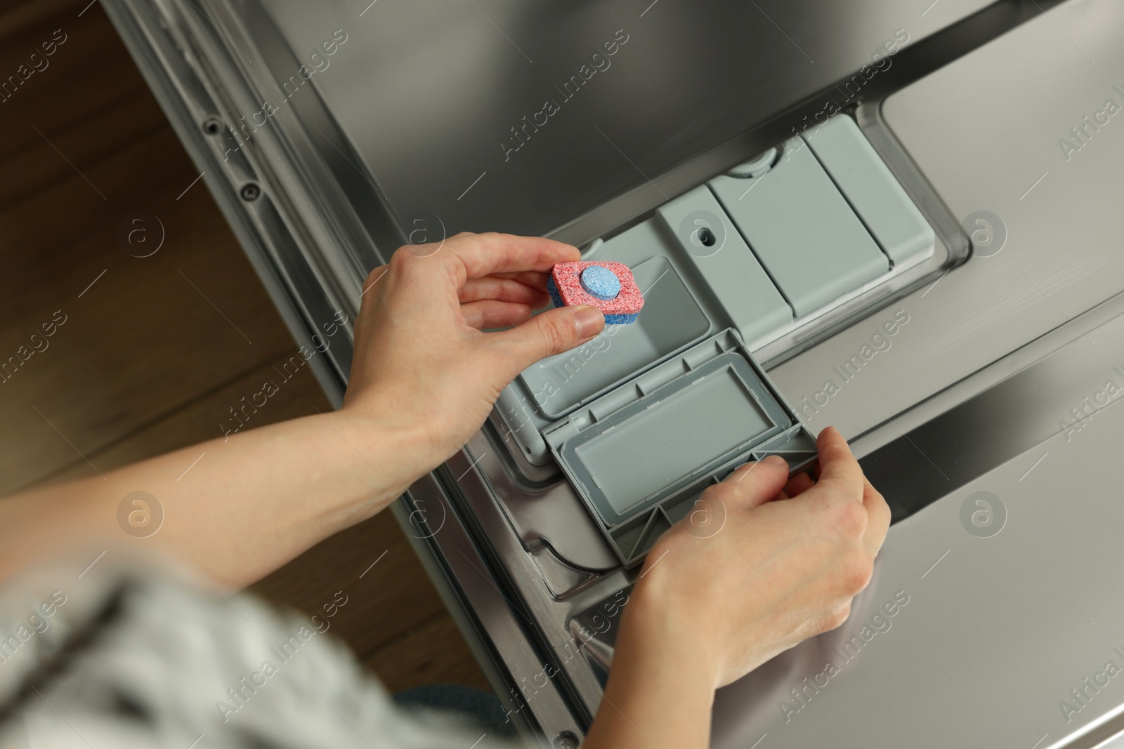 Photo of Woman putting detergent tablet into open dishwasher, above view