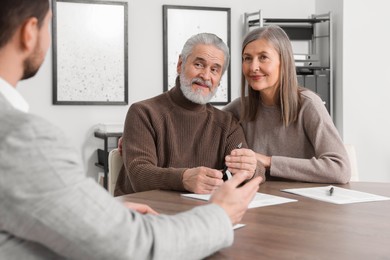 Elderly couple consulting insurance agent about pension plan at wooden table indoors