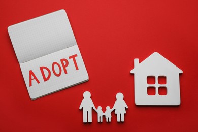 Photo of Family figure, house and open notebook with word Adopt on red background, flat lay