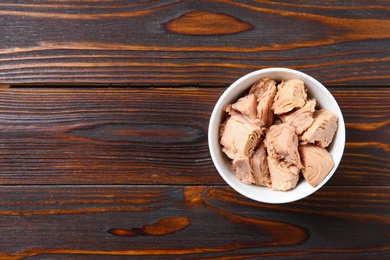 Photo of Bowl with canned tuna on wooden table, top view. Space for text