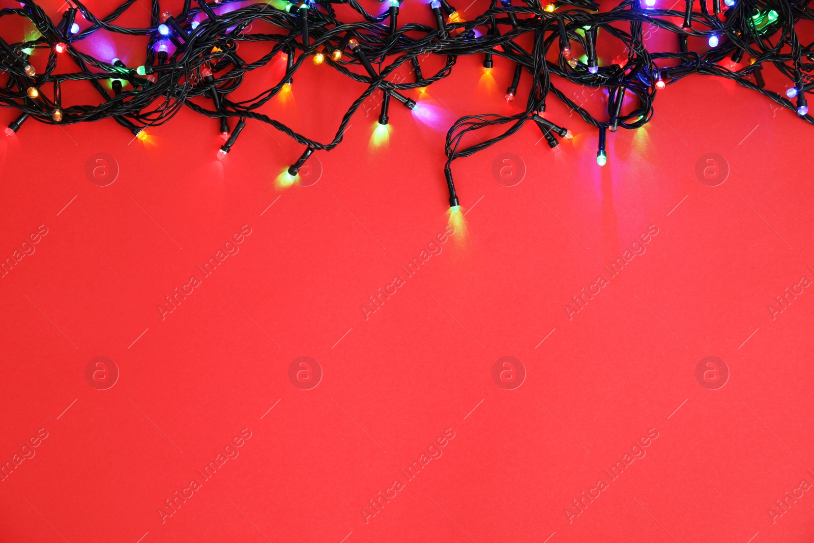 Photo of Glowing Christmas lights on color background, top view