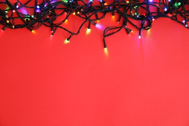 Photo of Glowing Christmas lights on color background, top view