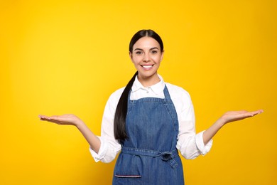 Photo of Young woman in blue jeans apron on yellow background