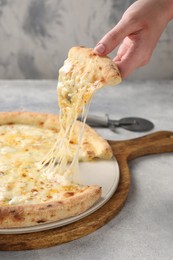 Photo of Woman taking piece of delicious cheese pizza at light grey table, closeup