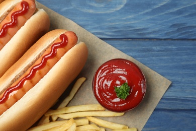 Composition with hot dogs, french fries and sauce on color wooden table, top view