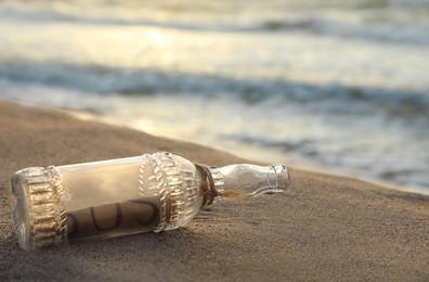 Photo of Glass bottle with SOS message on sand near sea, closeup