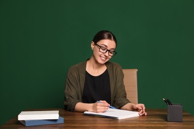 Portrait of young teacher at table against green background